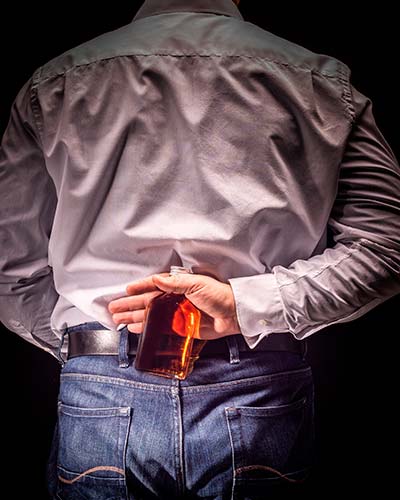 мужчина в рубашке держит бутылку алкоголя за спиной