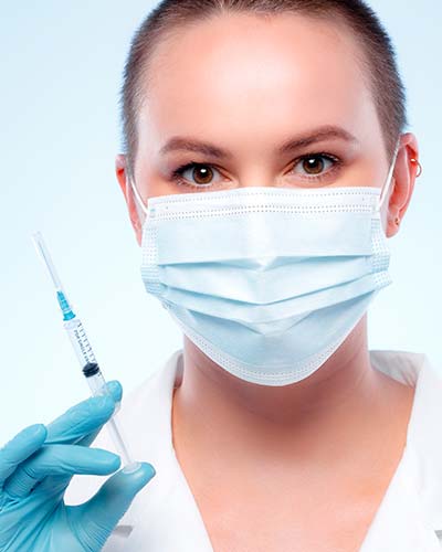 женщина врач в иедицинской маске со шприцом в руке